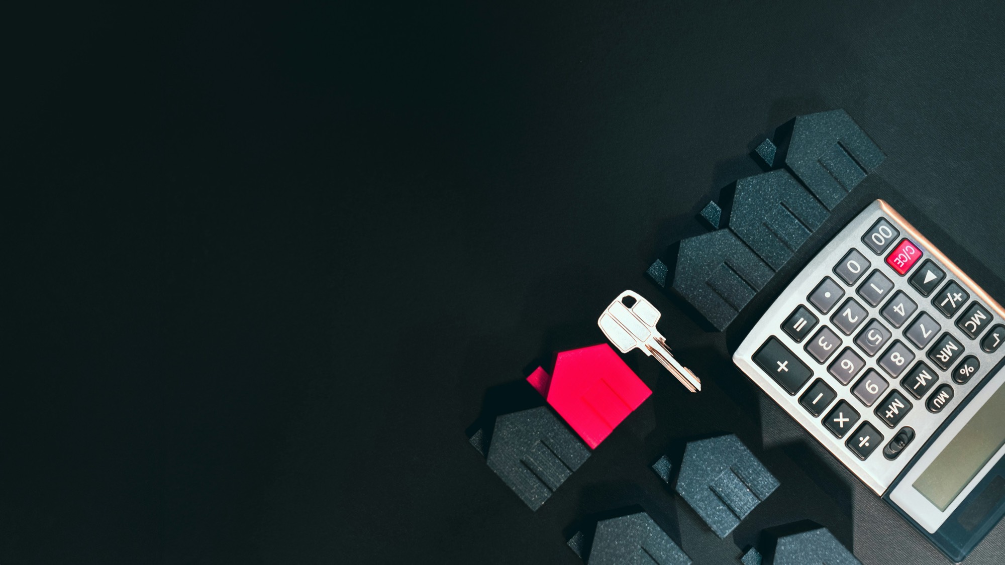 A house key and a small model house beside a calculator on a dark surface