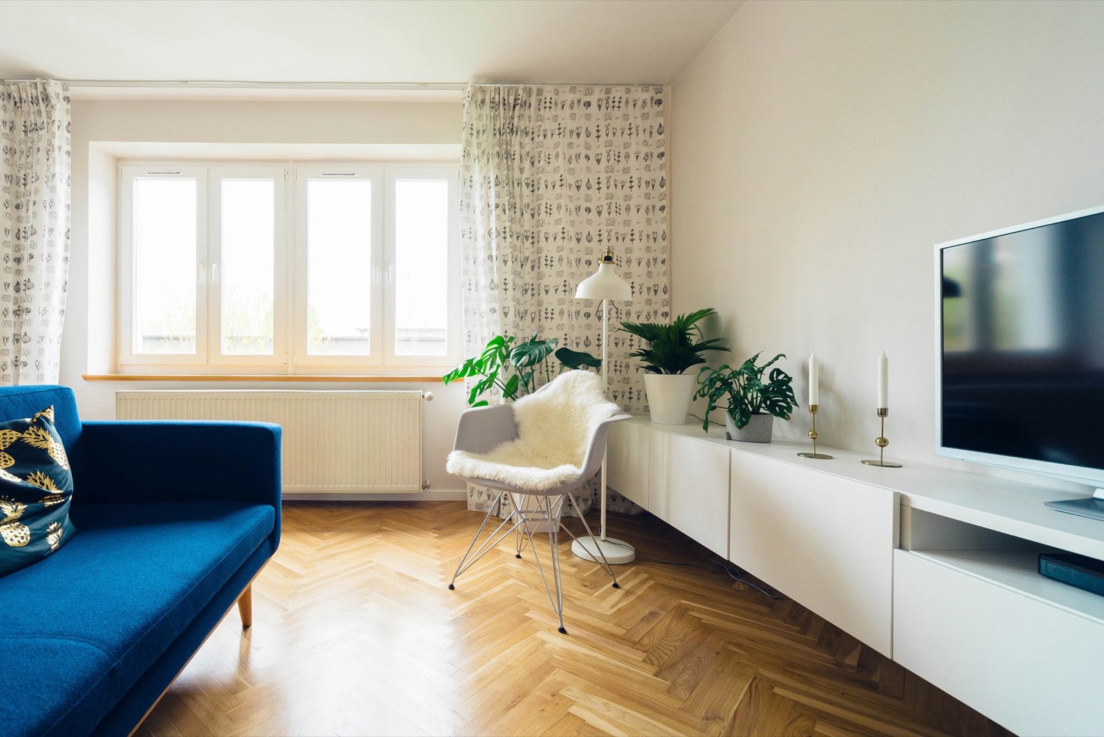 Bright rental living room with a blue sofa, herringbone wood floor, and plants by the window